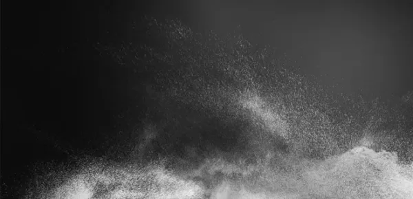 A burst of white powder or dust particles dispersing against a dark background, creating a cloud-like effect with varying densities and light.