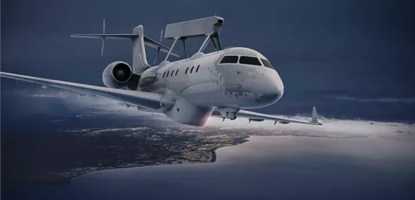 A military surveillance aircraft with a large radar mounted on top flies above a coastline at night, with city lights visible below and clouds in the background.
